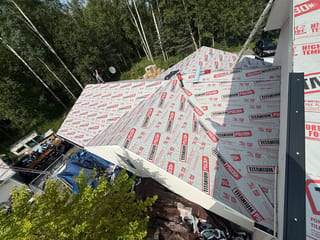 A Colonial-style house with a white metal roof under construction in a wooded area.