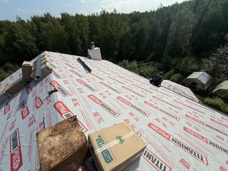 A metal roof being installed on a house in a forested area.