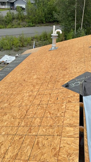 A modern home with a new metal roof installation in progress, surrounded by lush greenery.