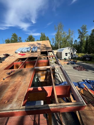 A metal roof being installed on a modern home with a forested rural setting.