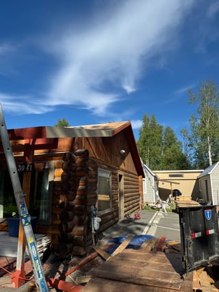 A metal roof being installed on a house with a brown exterior and a blue sky in the background.