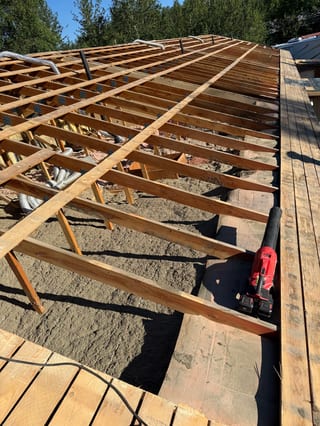A modern metal roof being installed on a single-family home in a forested area.