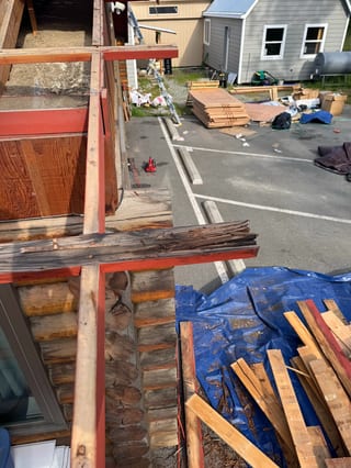 A metal roof being installed on a craftsman-style single-family home in a forested rural area on a sunny day.