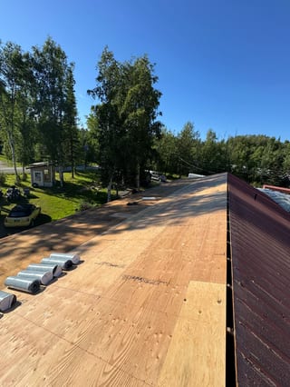 A new metal roof with a brownish-red colour, installed on a modern style single-family home in a suburban area with lush greenery and a golden hour sky.