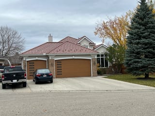 Aged Copper Interlock Shake aluminum roof on a brown house with dormers among tall pines, Calgary, Alberta
