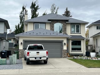 Charcoal Grey Interlock Slate aluminum roof on a two-storey home with dormers and stone accents among tall, Calgary, Alberta
