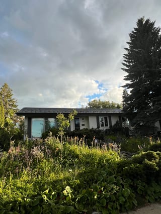 Charcoal Grey Interlock Slate aluminum roof on a white two-storey home with a metal roof among tall trees, Edmonton, Alberta