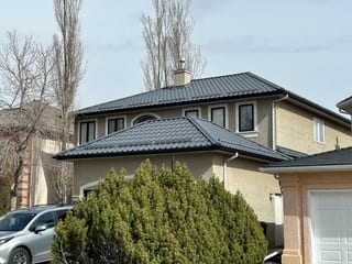 Charcoal Grey Interlock Tile aluminum roof on a tan one-storey home with solar panels and snow guards, Calgary, Alberta