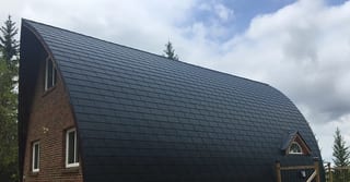 Black Interlock Slate aluminum roof on a brown single-family home with a metal roof among tall, Whitecourt, Alberta