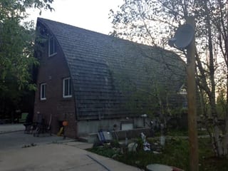 Black Interlock Slate aluminum roof on a brown single-storey home with a metal roof among trees, Whitecourt, Alberta