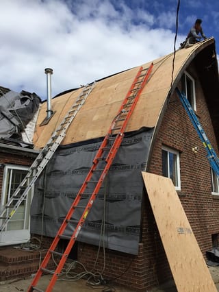 Black Interlock Slate aluminum roof being installed on a red brick home with a metal roof under construction in a, Whitecourt, Alberta