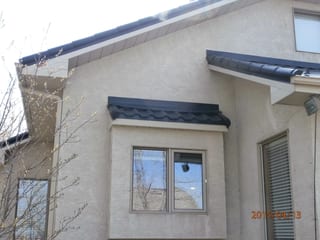 Black Interlock Tile aluminum roof on a beige single-storey home with dormers among tall pines, Redcliff, Alberta