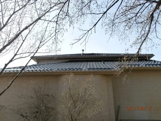Black Interlock Tile aluminum roof on a beige two-storey home with dormers among bare trees, Redcliff, Alberta