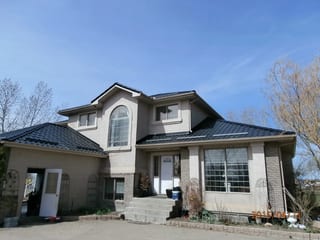 Black Interlock Tile aluminum roof on a beige house with a metal roof and two stories among tall, Redcliff, Alberta