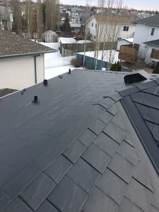 Deep Charcoal Interlock Slate aluminum roof on a white single-storey home with dormers among tall trees, Fort Saskatchewan, Alberta