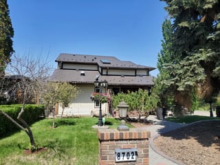Tudor Brown Interlock Cedar Shingle aluminum roof on a Tudor style home with a brown roof among trees and a blue, Edmonton, Alberta