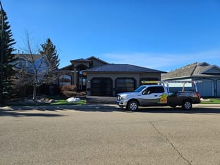 Black Interlock Slate aluminum roof being installed on a single-family home with a grey roof among urban buildings, Red Deer, Alberta