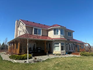 Tile Red Interlock Slate aluminum roof on a tan two-storey home with dormers among tall pines, Foothills County, Alberta