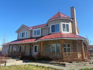 Tile Red Interlock Slate aluminum roof on a tan stone house with a red metal roof in a rural area, Foothills County, Alberta