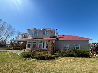 Tile Red Interlock Slate aluminum roof on a beige one-storey home with a red metal roof in a rural, Foothills County, Alberta