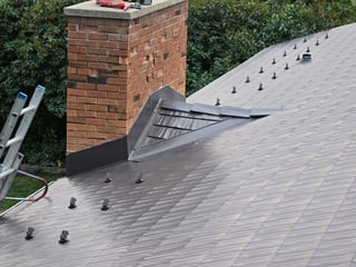 Tudor Brown Interlock Cedar Shingle aluminum roof being installed on a colonial-style home with a metal roof under construction, Rocky Mountain House, Alberta