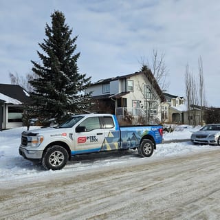 Deep Charcoal Interlock Cedar Shingle aluminum roof on a two-storey home with dormers among snow-covered trees, Crossfield, Alberta