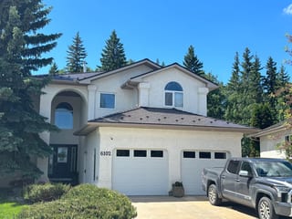 Tudor Brown Interlock Cedar Shingle aluminum roof on a white two-storey home with dormers among tall pines, Grande Prairie, Alberta
