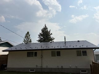 Deep Charcoal Interlock Slate aluminum roof on a white ranch-style home with a metal roof among tall trees, Coleman, Alberta