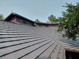 Musket Grey Interlock Shake aluminum roof on a red two-storey home with dormers among tall trees, Warner, Alberta