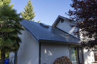 Deep Charcoal Interlock Slate aluminum roof on a white modern home with a metal roof among lush greenery, Sechelt, British Columbia
