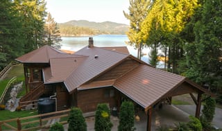 Aged Copper Interlock Cedar Shingle aluminum roof on a brown chalet with dormers on a waterfront property among, Sechelt, British Columbia