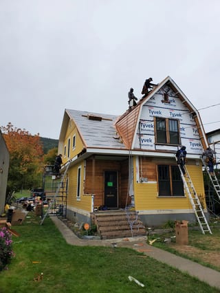 Copper Penny Interlock Cedar Shingle aluminum roof being installed on a yellow two-storey cottage with a metal roof under, Lumby, British Columbia