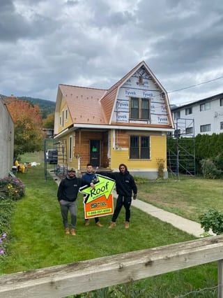 Copper Penny Interlock Cedar Shingle aluminum roof being installed on a yellow home with a dormer and two storeys in a forested, Lumby, British Columbia