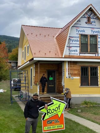 Copper Penny Interlock Cedar Shingle aluminum roof on a yellow two-storey home with dormers among tall pines, Lumby, British Columbia
