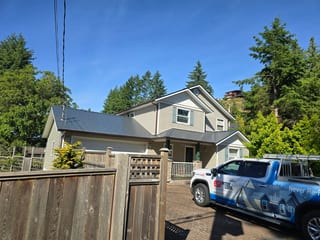 Deep Charcoal Interlock Slate aluminum roof on a beige two-storey home with dormers among tall conifers, Gibsons, British Columbia