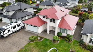 Tile Red Interlock Shingle aluminum roof on a white two-storey home with red roof among greenery, Surrey, British Columbia