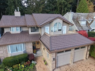 Colonial Brown Interlock Shake aluminum roof on a beige two-storey home with a dormer among tall trees, North Vancouver, British Columbia