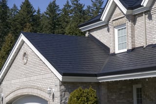 Black Interlock Slate aluminum roof on a grey two-storey Craftsman home with dormers among tall, Surrey, British Columbia