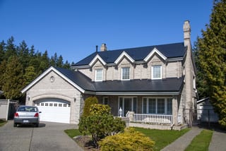 Black Interlock Slate aluminum roof on a tan two-storey Colonial home with a metal roof among tall, Surrey, British Columbia