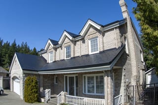 Black Interlock Slate aluminum roof on a beige two-storey Colonial home with dormers and a chimney, Surrey, British Columbia