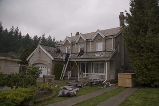Black Interlock Slate aluminum roof being installed on a two-storey house with a dormer and skylight among tall, Surrey, British Columbia