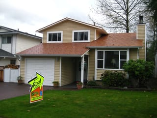 Aged Copper Interlock Slate aluminum roof on a yellow two-storey home with dormers among tall pines, Coquitlam, British Columbia