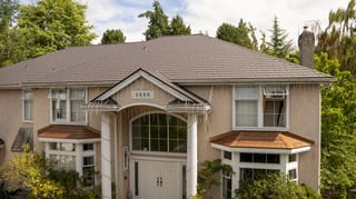 Tudor Brown Interlock Slate aluminum roof on a Tudor-style home with a brown metal roof among tall trees, Surrey, British Columbia