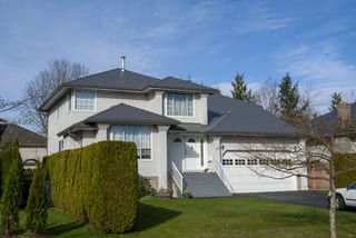 Musket Grey Interlock Slate aluminum roof on a two-storey home with a grey metal roof among tall trees, Surrey, British Columbia
