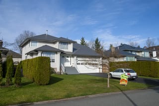 Musket Grey Interlock Slate aluminum roof on a two-storey white home with dormers among tall pines, Surrey, British Columbia