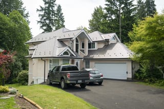 Weathered Interlock Slate aluminum roof on a white two-storey home with a metal roof among tall trees, Port Coquitlam, British Columbia