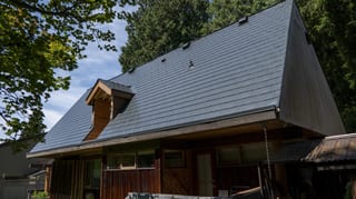 Deep Charcoal Interlock Slate aluminum roof on a brown A-frame home with a metal roof among tall trees, Burnaby, British Columbia