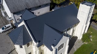 Deep Charcoal Interlock Slate aluminum roof on a white single-family home with a metal roof and tall trees, Vancouver, British Columbia