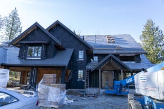 Musket Grey Interlock Slate aluminum roof being installed on a two-storey home with dormers among tall pines and fir, Abbotsford, British Columbia