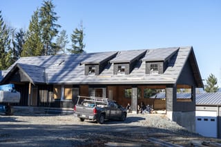 Musket Grey Interlock Slate aluminum roof being installed on a metal roof on a single-storey rural home among tall pines, Abbotsford, British Columbia